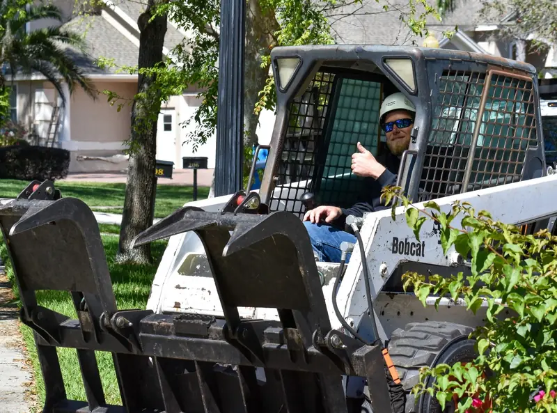 Eli giving a thumbs up from a Bobcat skid steer with a grapple attachment